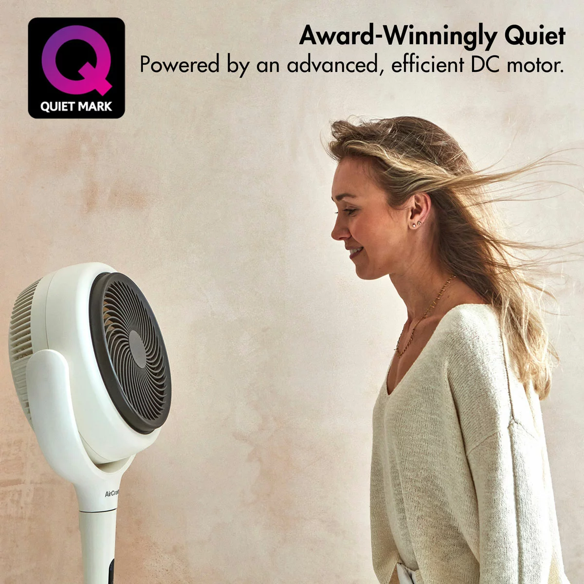 Compact stone white AirCraft LUME MIDI table air circulator fan resting on a bedside wooden nightstand with its dimmable ambient backlight softly glowing.
