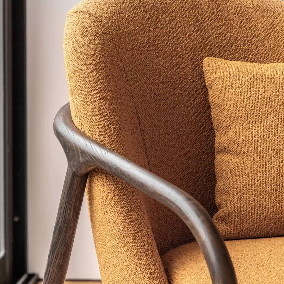 A front-three-quarter view of the Gallery Alegra ochre fabric armchair, showcasing its curved dark wood frame and vibrant textured yellow cushions in a modern living room corner.