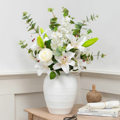 The Artificial Lily & Rose Bouquet in Vase displayed on a flat surface, showcasing vibrant fabric lilies and roses mixed with eucalyptus leaves inside a sleek white bowl.