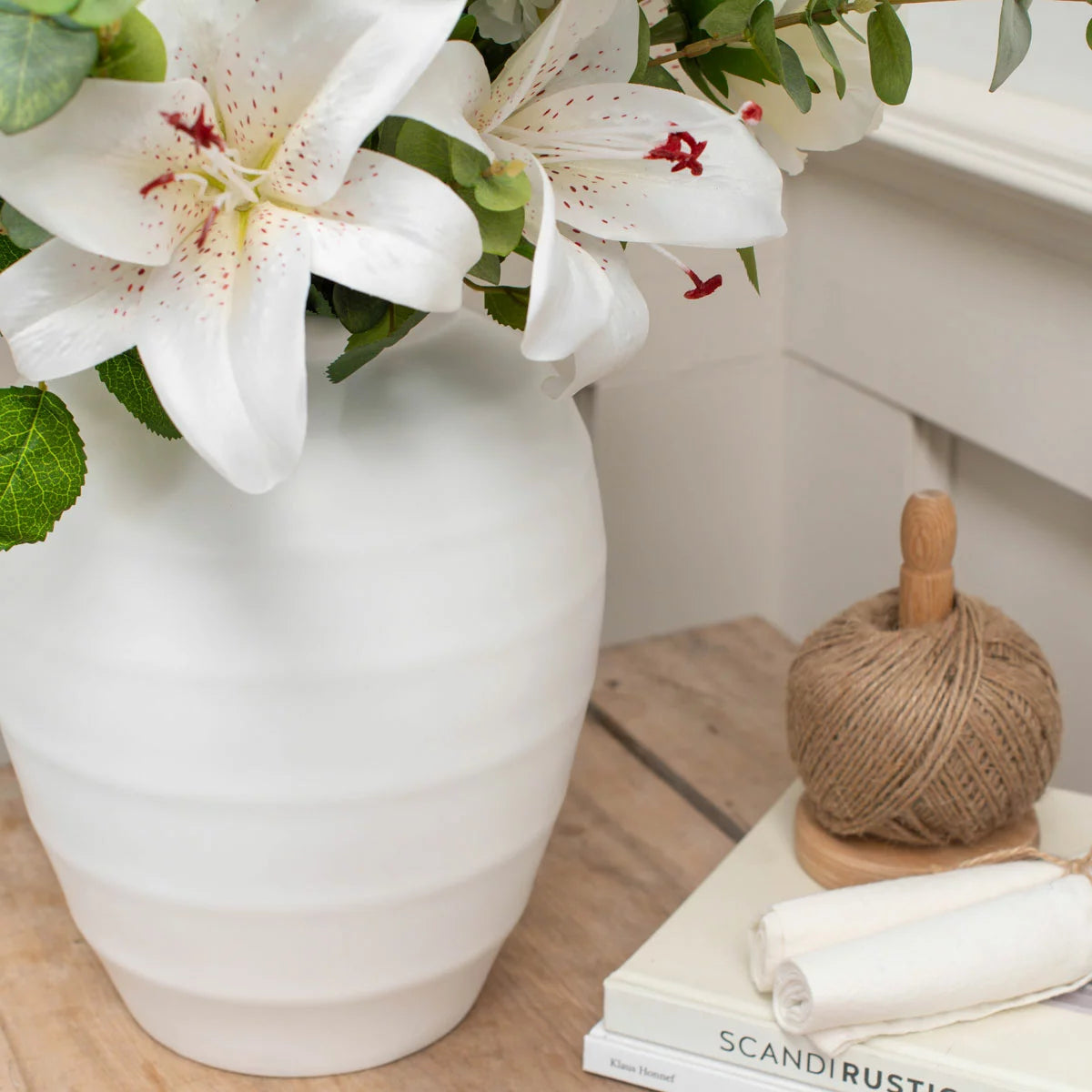 The Artificial Lily & Rose Bouquet in Vase displayed on a flat surface, showcasing vibrant fabric lilies and roses mixed with eucalyptus leaves inside a sleek white bowl.