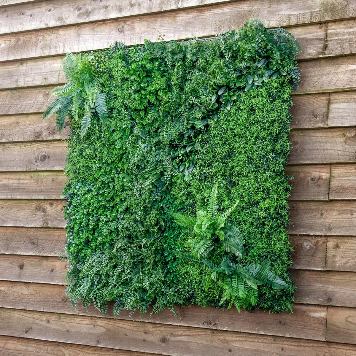 Close-up of deep green artificial mixed foliage panel featuring ivy and fern leaves mounted on an outdoor brick patio wall.