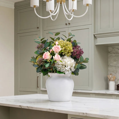 Front view of artificial summer bouquet featuring white roses and hydrangeas with eucalyptus leaves in a sleek white bowl vase on a wooden table.