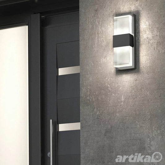 A vertical matte black Artika Mazza wall light with a frosted white diffuser illuminated against a modern dark gray exterior wall.