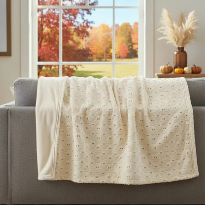 Ashford Home Embroidered Halloween throw blanket in white plush faux fur featuring stitched orange pumpkins folded over a charcoal sofa arm.