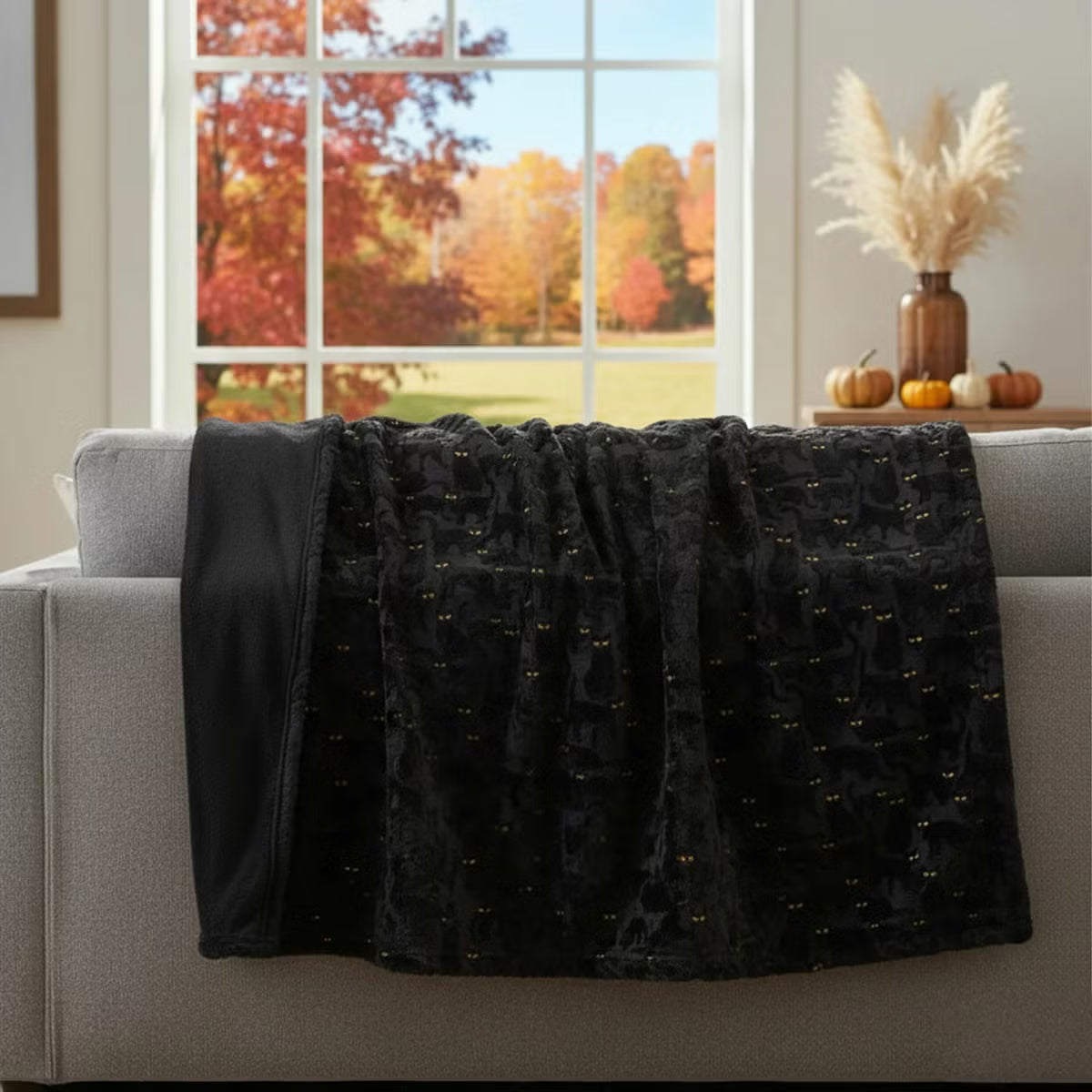 Ashford Home Embroidered Halloween throw blanket in white plush faux fur featuring stitched orange pumpkins folded over a charcoal sofa arm.