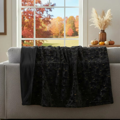 Ashford Home Embroidered Halloween throw blanket in white plush faux fur featuring stitched orange pumpkins folded over a charcoal sofa arm.