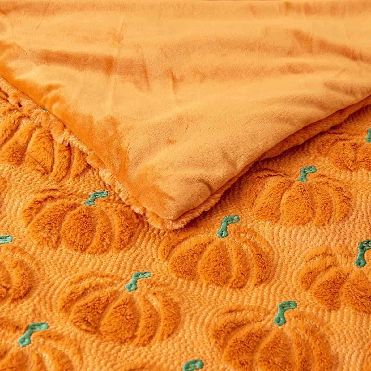 Ashford Home Embroidered Halloween throw blanket in white plush faux fur featuring stitched orange pumpkins folded over a charcoal sofa arm.