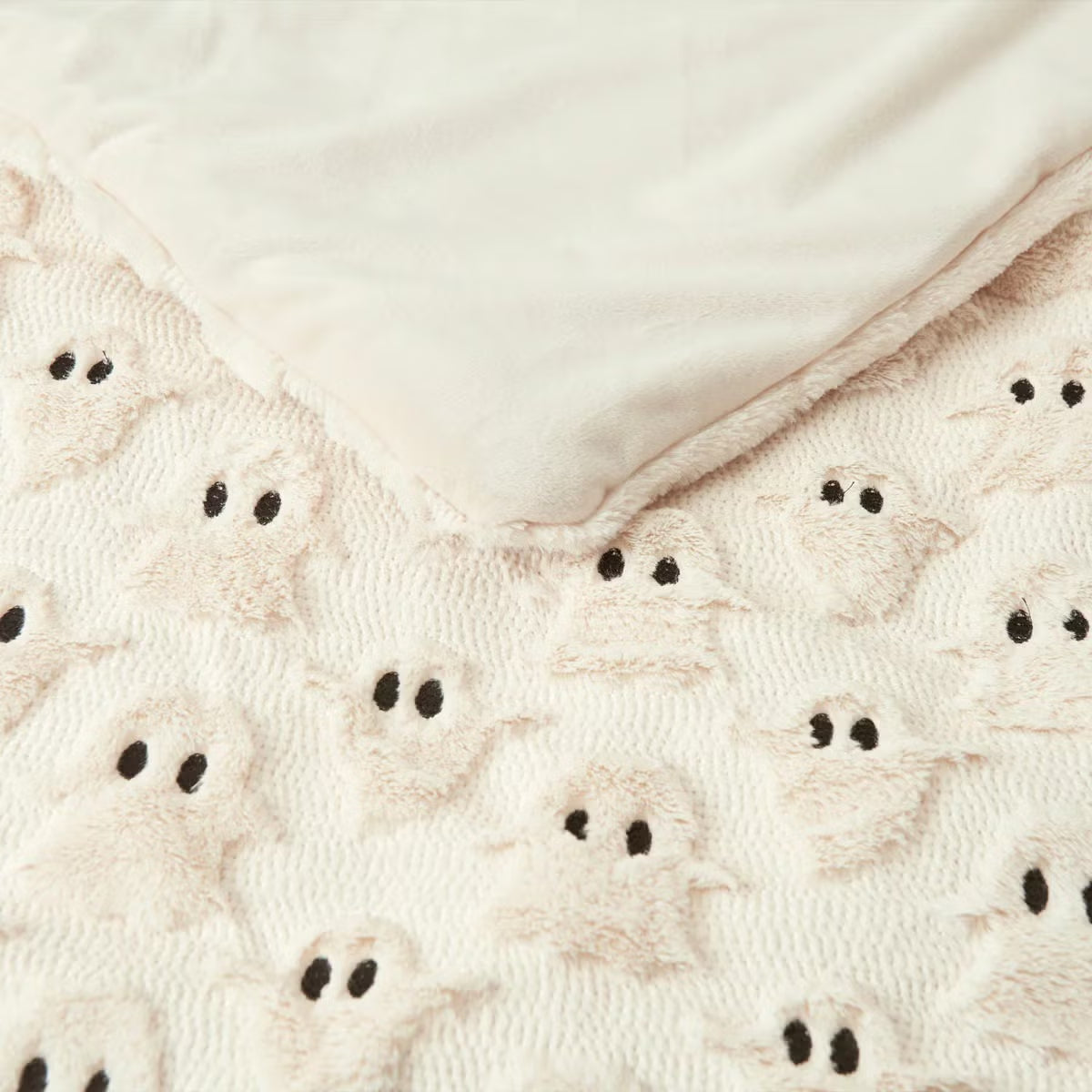 Ashford Home Embroidered Halloween throw blanket in white plush faux fur featuring stitched orange pumpkins folded over a charcoal sofa arm.