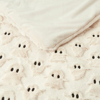 Ashford Home Embroidered Halloween throw blanket in white plush faux fur featuring stitched orange pumpkins folded over a charcoal sofa arm.