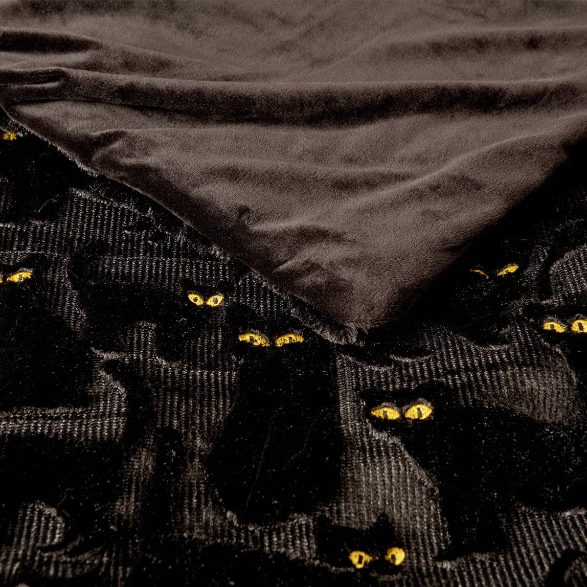 Ashford Home Embroidered Halloween throw blanket in white plush faux fur featuring stitched orange pumpkins folded over a charcoal sofa arm.