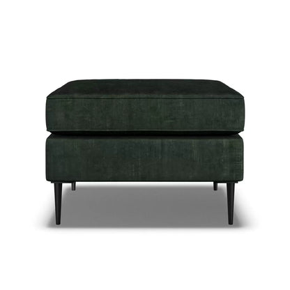 Top-angle view of the Aspen Green Velvet Footstool featuring rich emerald upholstery and sleek 18 cm black metal legs in a brightly lit modern living room setup.
