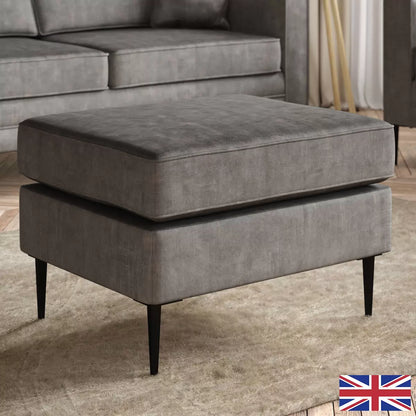 Top angle view of the Aspen Grey Velvet Footstool with distressed texture, piped border, and slim black metal stiletto legs in a modern lounge setting.