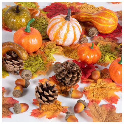 Textured orange, green, and mini artificial pumpkins paired with fabric autumn leaves and pine cones arranged neatly on a wooden table setting.