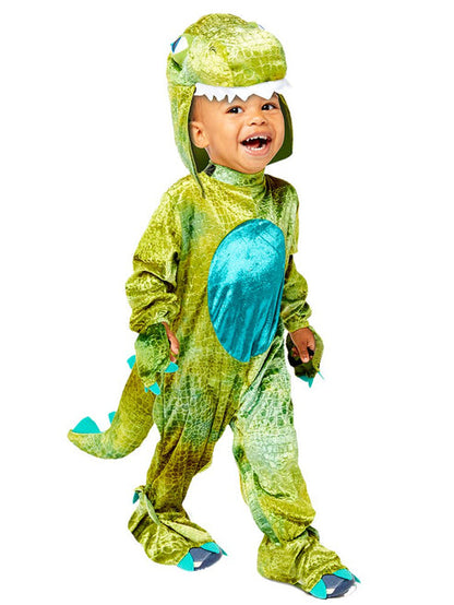 Front view of a toddler wearing a soft green scale-patterned dinosaur jumpsuit with a plush hood and yellow velour belly panel in a bright living room.