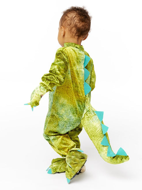 Front view of a toddler wearing a soft green scale-patterned dinosaur jumpsuit with a plush hood and yellow velour belly panel in a bright living room.