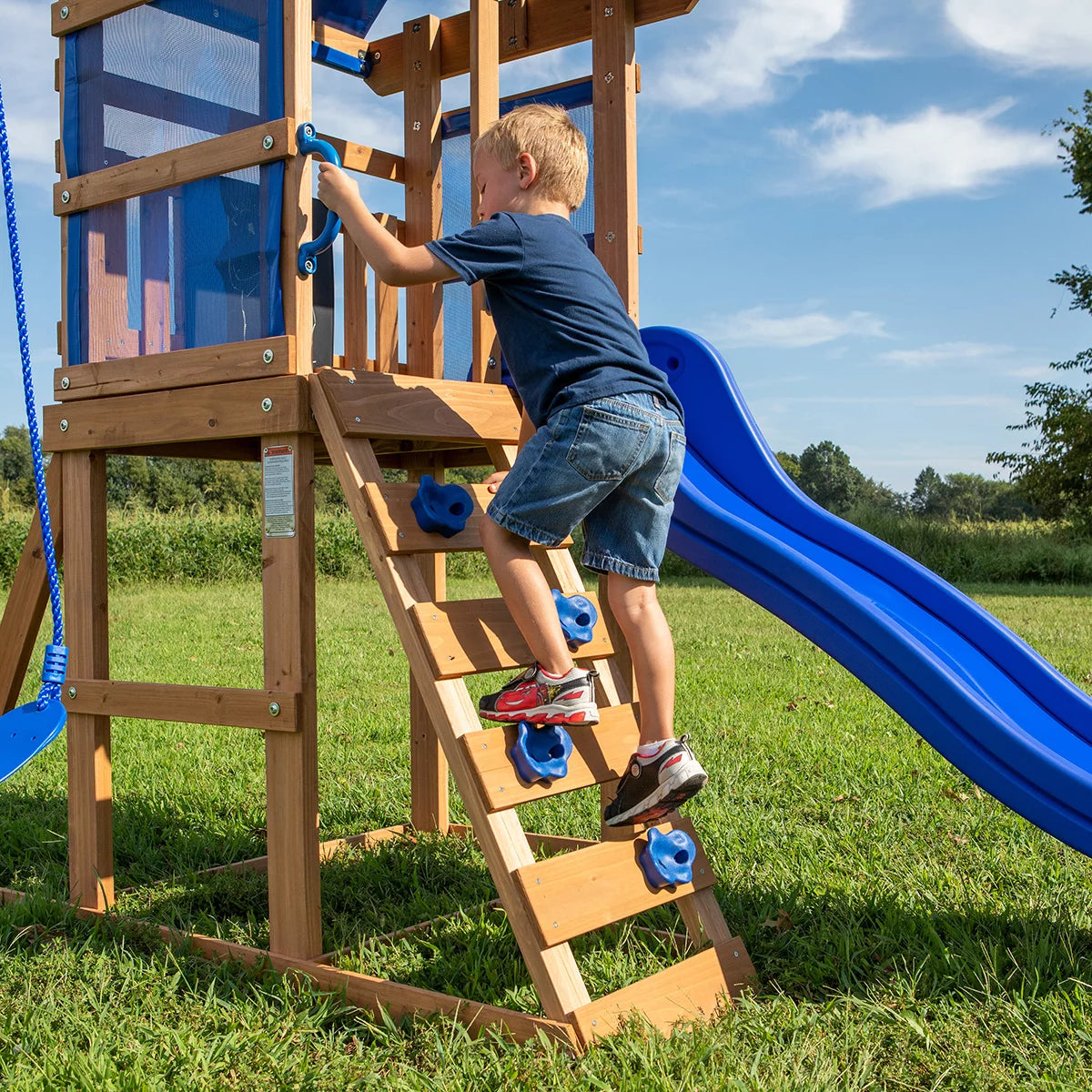 Backyard Discovery Aurora brown cedar wood swingset playcentre with canopy roof, rock wall ladder, wave slide, chalkboard, and garden swing area for children.