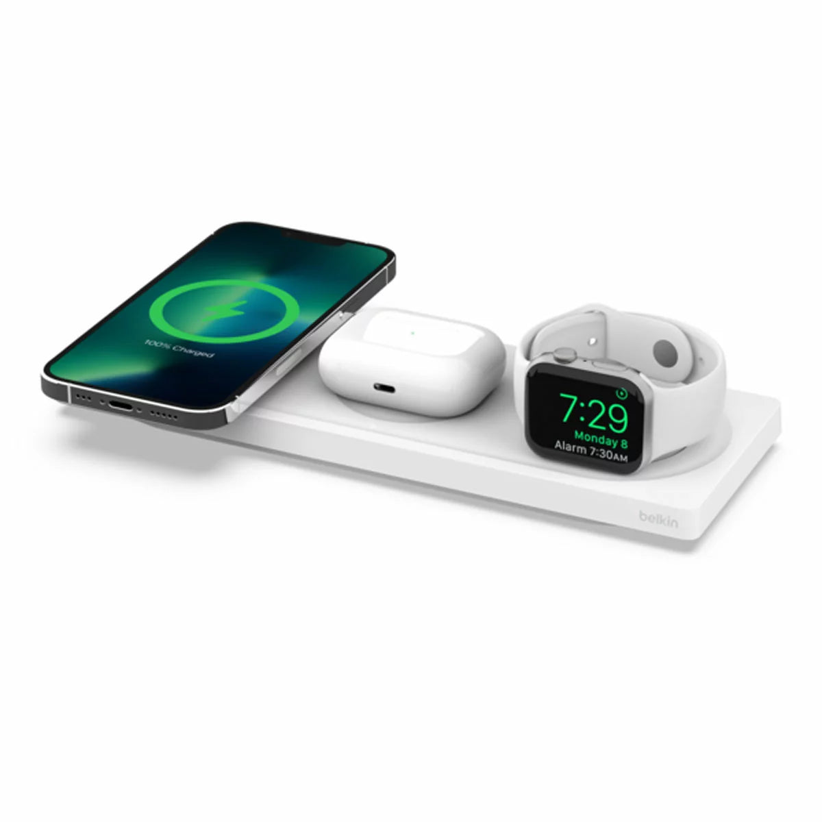 Top-down view of a white flat Belkin 3-in-1 MagSafe charging pad on a wooden table, simultaneously holding a modern smartphone, a smartwatch, and a wireless earbud case.