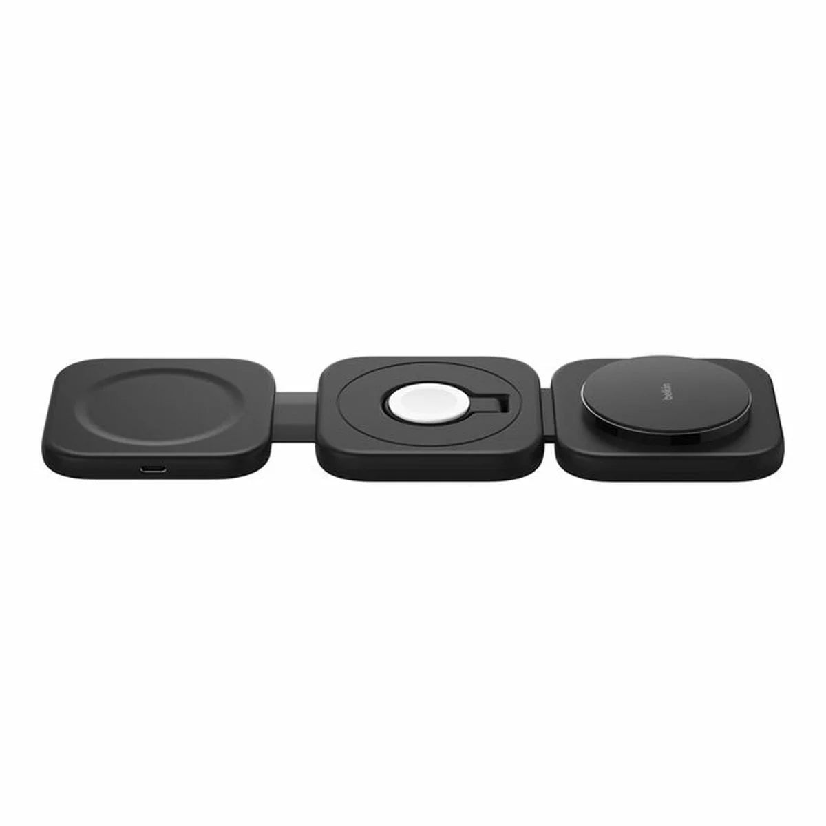 A black foldable Belkin BoostCharge Pro 3-in-1 charging pad laid out flat on a hotel desk, wirelessly charging an iPhone, Apple Watch, and AirPods case.