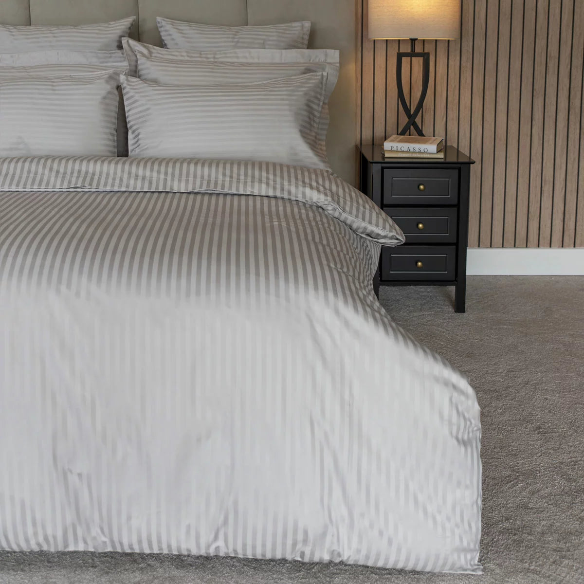 Close-up flat lay of the Belledorm 540 thread count grey satin stripe duvet cover showing the silky woven texture and matching pillowcase in a brightly lit modern bedroom.