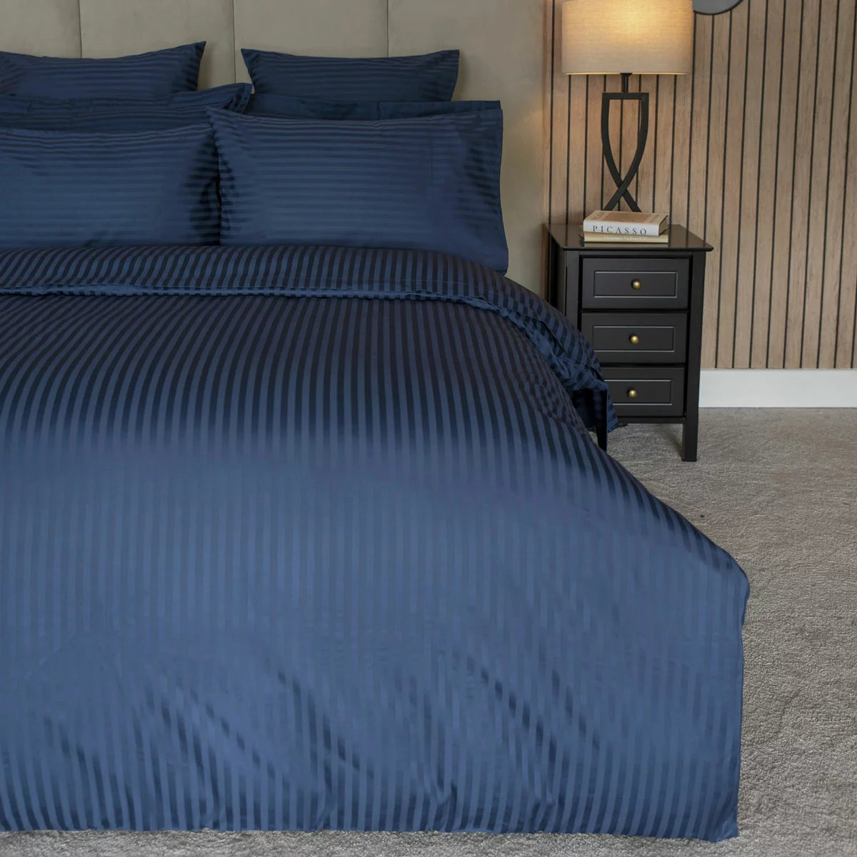 Flat lay image of the Belledorm 540 thread count navy satin stripe duvet cover set with matching pillowcases neatly arranged on a modern wooden bed.