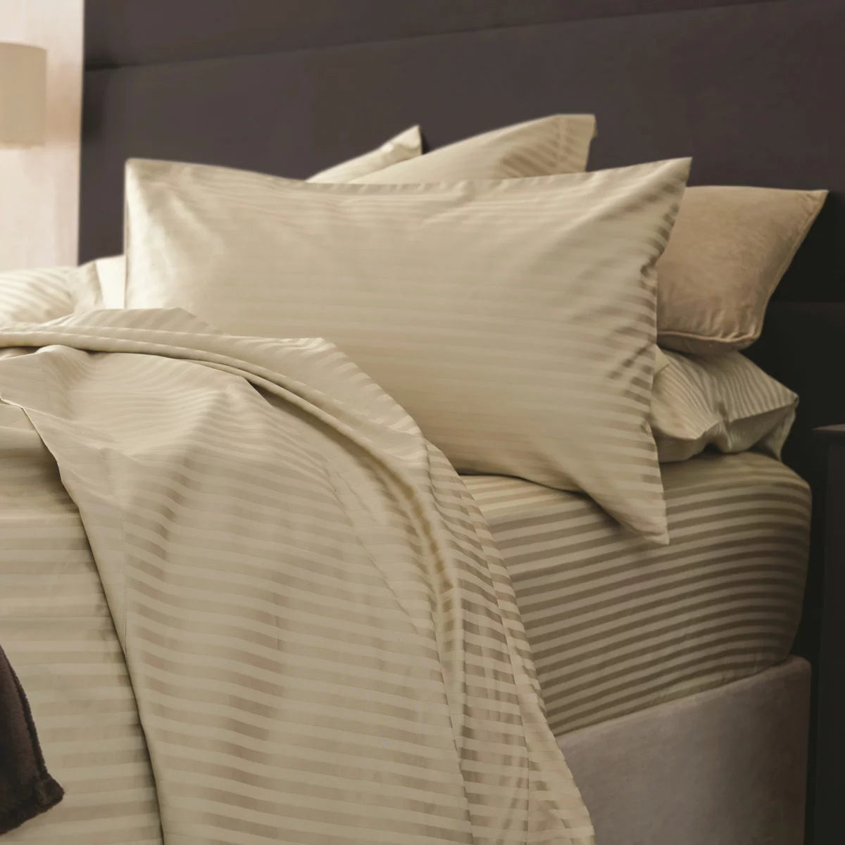 Flat lay image of the Belledorm 540 thread count taupe satin stripe duvet cover set with matching pillowcases neatly laid out on a neutral wooden bedframe.