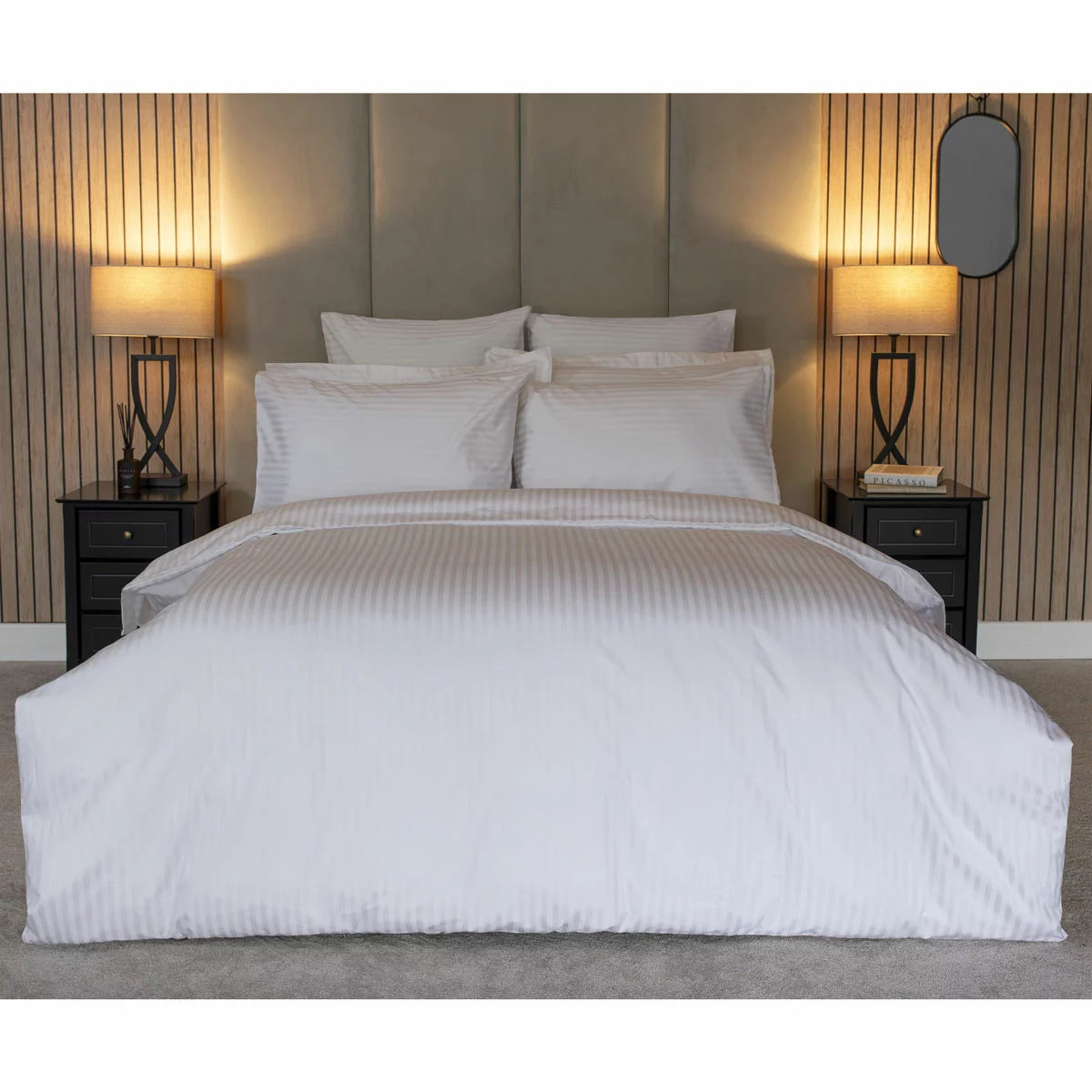 Neat arrangement of the Belledorm 540 thread count white satin stripe duvet cover set with matching pillowcases folded on a minimalist wooden bed frame.