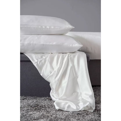 Pair of Belledorm 100% Mulberry silk ivory housewife pillowcases neatly laid out on a plush mattress, highlighting the soft lustrous fabric finish.