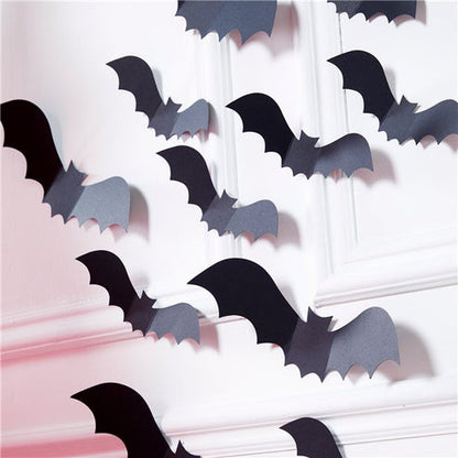 Matte black 3D paper bat cutouts in various sizes arranged on a white wall in a flying swarm pattern.