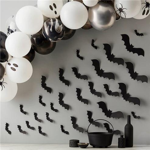 Matte black 3D paper bat cutouts in various sizes arranged on a white wall in a flying swarm pattern.