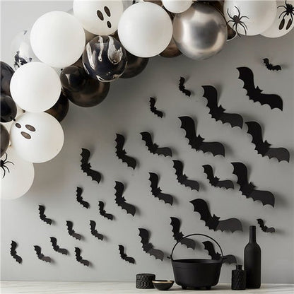 Matte black 3D paper bat cutouts in various sizes arranged on a white wall in a flying swarm pattern.