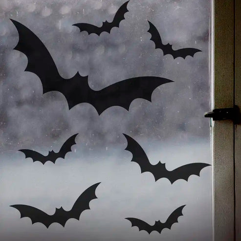 A set of nine black bat static cling window stickers arranged on a clear glass pane during a Halloween home setup.