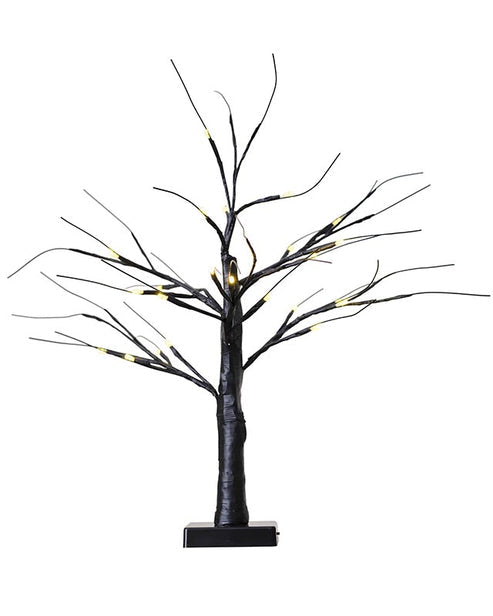 A small, matte black decorative tree with glowing warm white LED lights on the branches, sitting illuminated on a modern wooden entryway table.