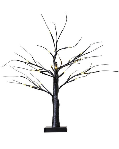 A small, matte black decorative tree with glowing warm white LED lights on the branches, sitting illuminated on a modern wooden entryway table.