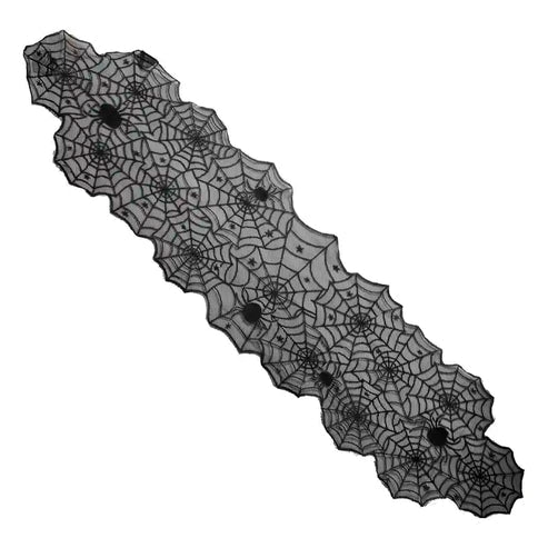 Top-down view of a black spider web lace table runner laid across a light wooden dining table with rustic Halloween decorations.