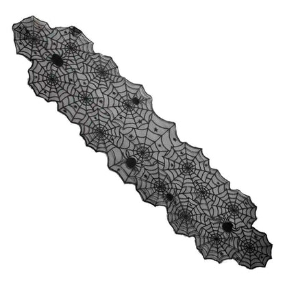 Top-down view of a black spider web lace table runner laid across a light wooden dining table with rustic Halloween decorations.
