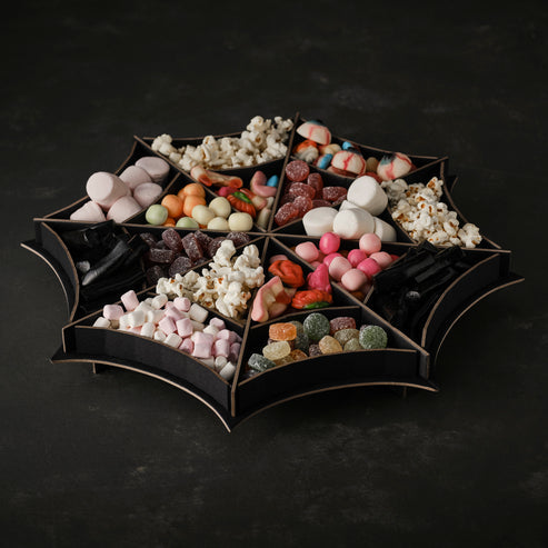 Matte black spider web tiered treat stand holding Halloween cupcakes on a dark party display table.