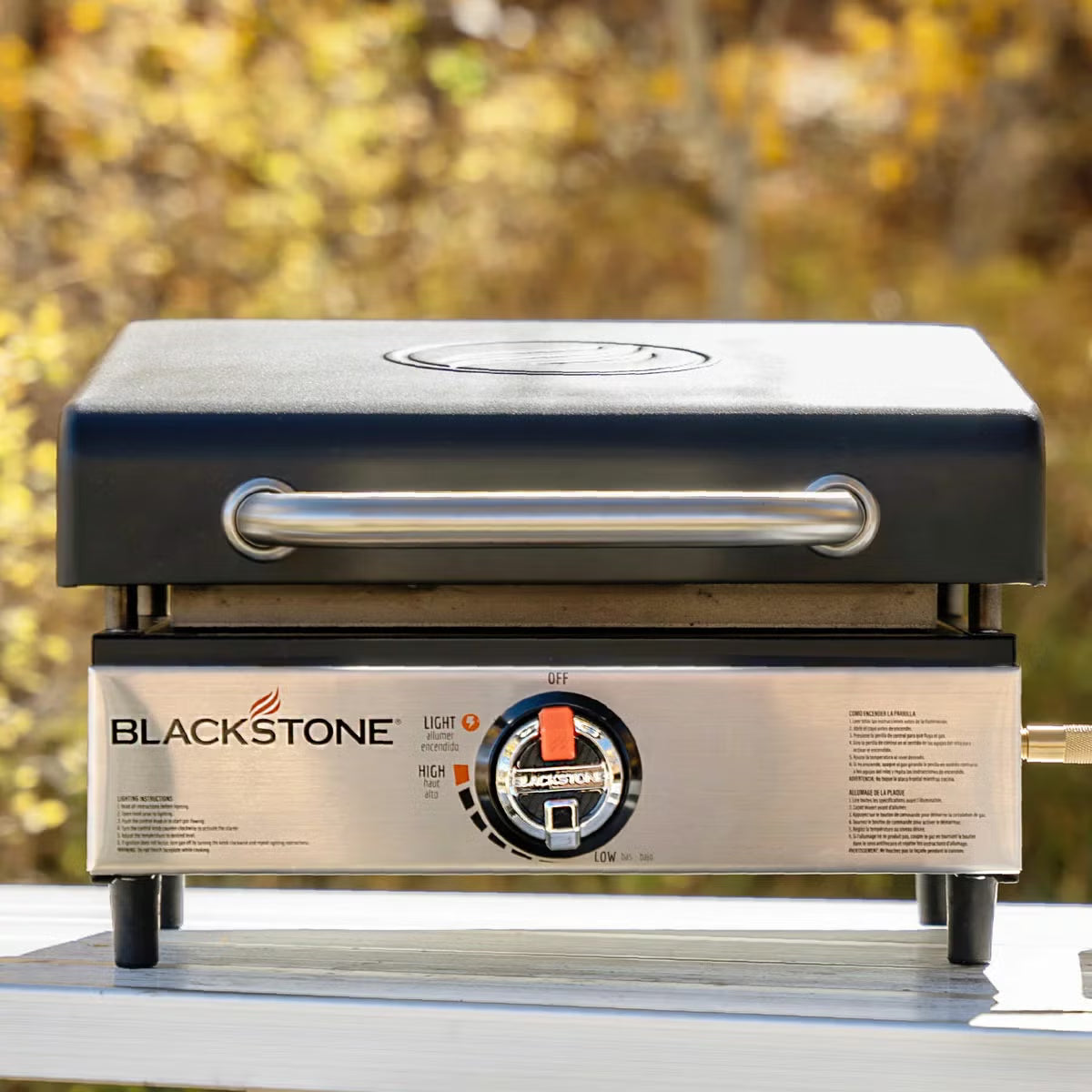 Angle view of the black Blackstone 17 inch tabletop gas griddle with open hood standing on an outdoor wooden table.