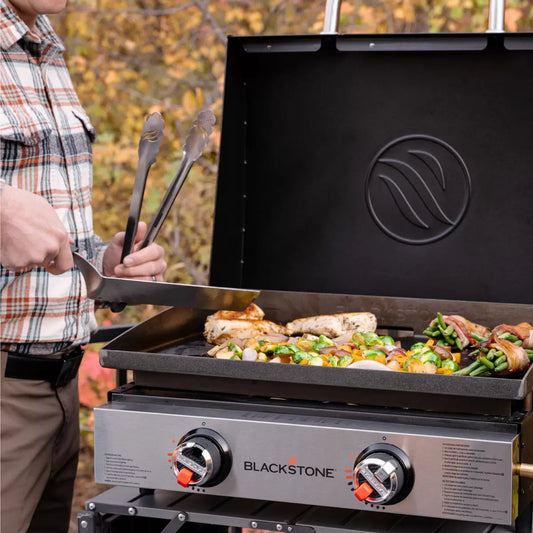 Blackstone 22 inch Table Top Griddle Bundle with hood and accessories on a wooden picnic table.