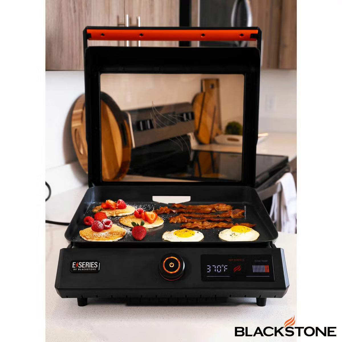 Front view of the black Blackstone E-Series 17 inch electric griddle on a kitchen counter showing the digital LCD screen, glass hood window, and smooth ceramic plate.