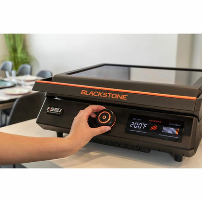 Front view of the black Blackstone E-Series 17 inch electric griddle on a kitchen counter showing the digital LCD screen, glass hood window, and smooth ceramic plate.
