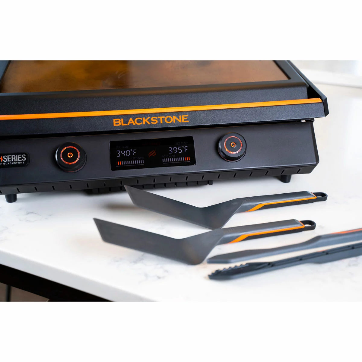 A Blackstone E-Series 17" electric griddle in a modern kitchen setting, showing the sleek glass hood, digital LCD control panel, and large non-stick ceramic cooking surface.