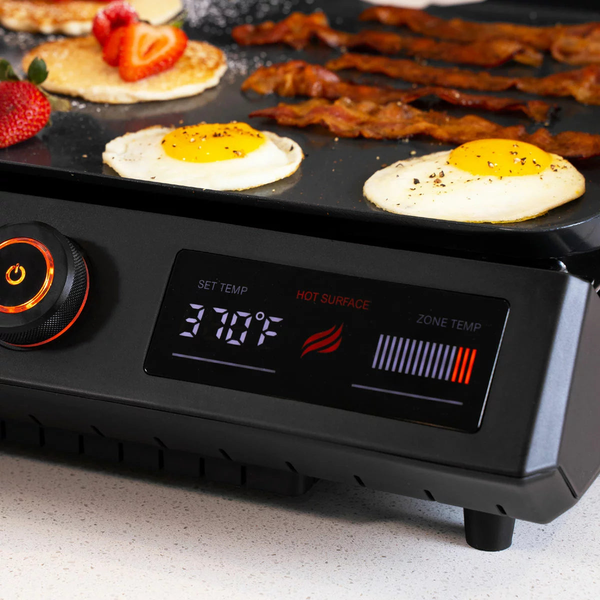 A Blackstone E-Series 17" electric griddle in a modern kitchen setting, showing the sleek glass hood, digital LCD control panel, and large non-stick ceramic cooking surface.