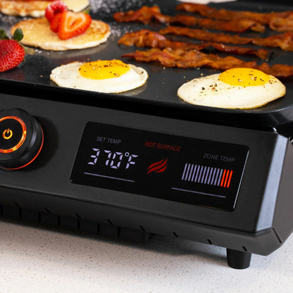 A Blackstone E-Series 17" electric griddle in a modern kitchen setting, showing the sleek glass hood, digital LCD control panel, and large non-stick ceramic cooking surface.