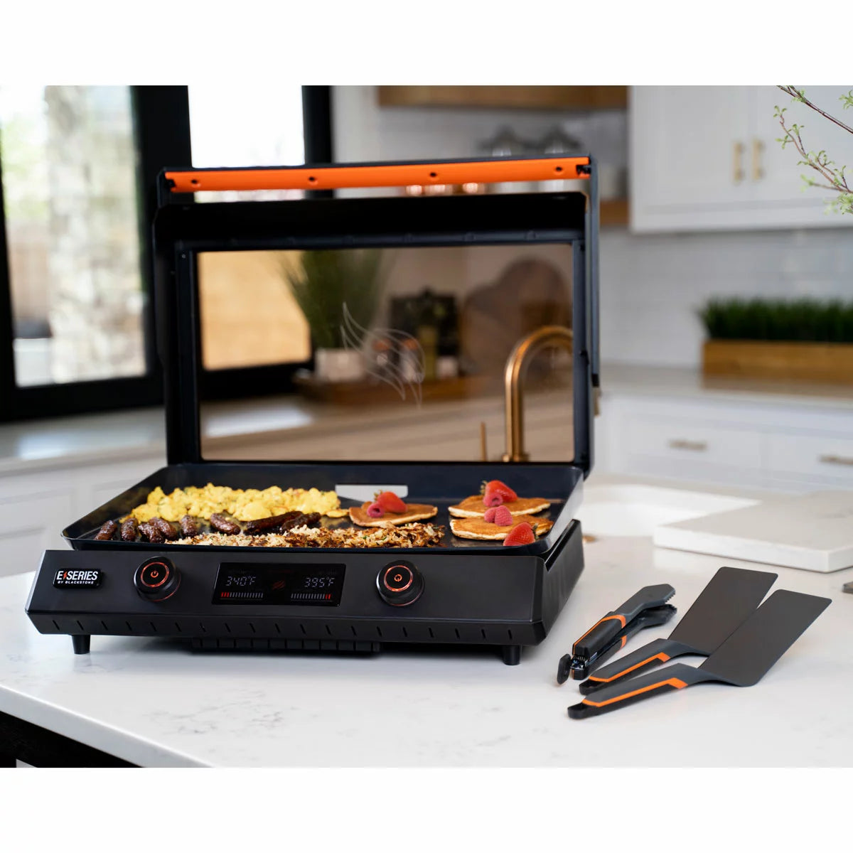 The Blackstone E-Series 22" Electric Griddle with its sleek glass hood and digital control panel, set up on a modern kitchen counter with cooked food ready to serve.