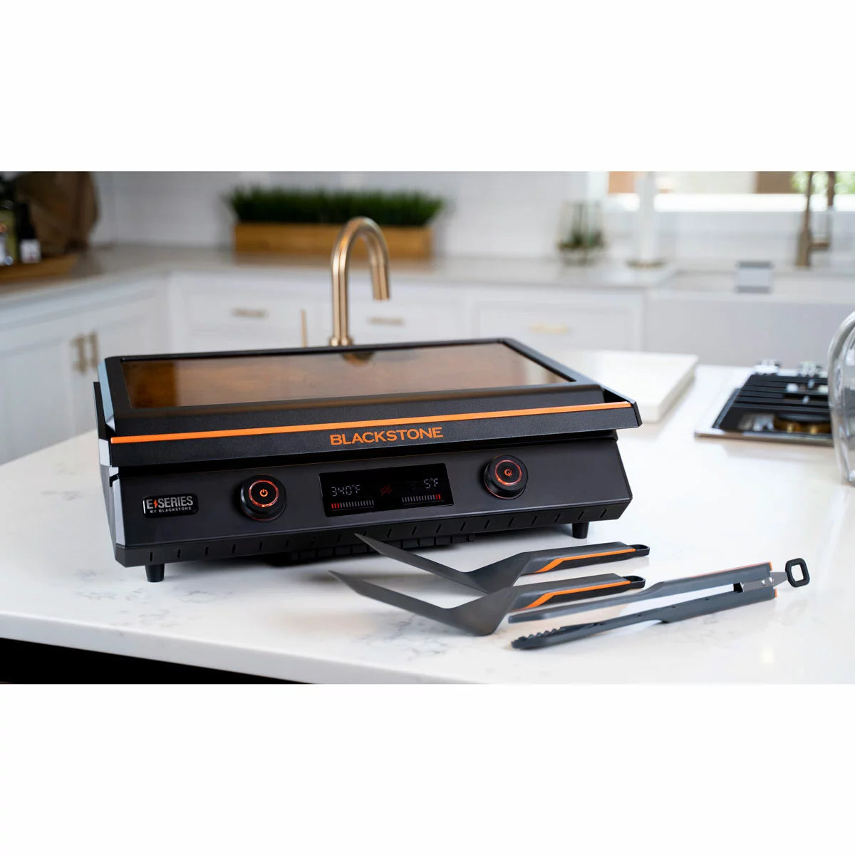 The Blackstone E-Series 22" Electric Griddle with its sleek glass hood and digital control panel, set up on a modern kitchen counter with cooked food ready to serve.