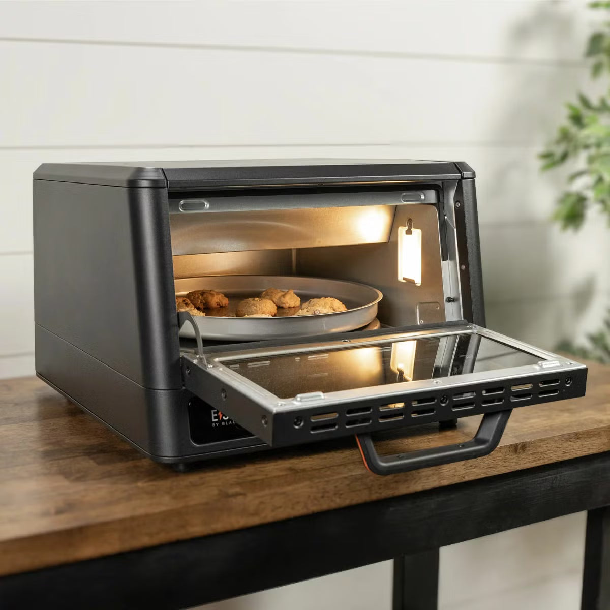 Front view of the black Blackstone E-Series electric pizza and air fryer oven sitting on a kitchen counter displaying its touchscreen control panel and open glass door with a 14 inch rotating deck inside.