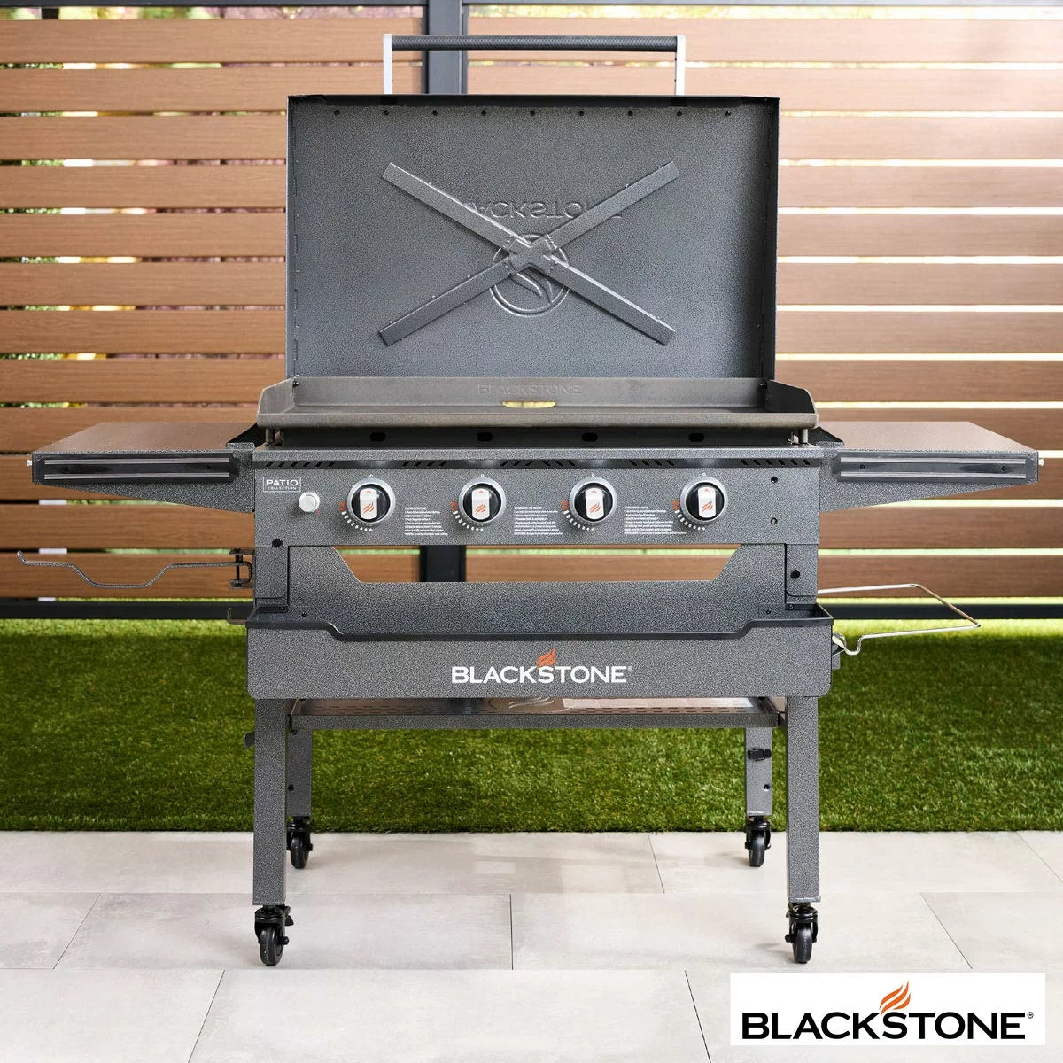 Blackstone Omnivore 36" Griddle with hood open, showing the spacious raw steel cooking surface and integrated front accessory shelves on a patio.