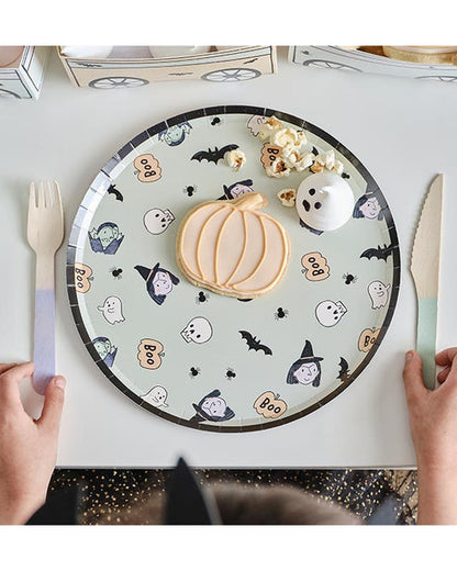 A stack of colorful ghost-patterned Boo Crew paper plates arranged neatly on a dark wooden Halloween buffet table next to seasonal treats.