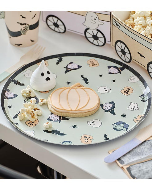 A stack of colorful ghost-patterned Boo Crew paper plates arranged neatly on a dark wooden Halloween buffet table next to seasonal treats.