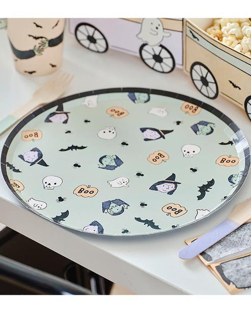 A stack of colorful ghost-patterned Boo Crew paper plates arranged neatly on a dark wooden Halloween buffet table next to seasonal treats.